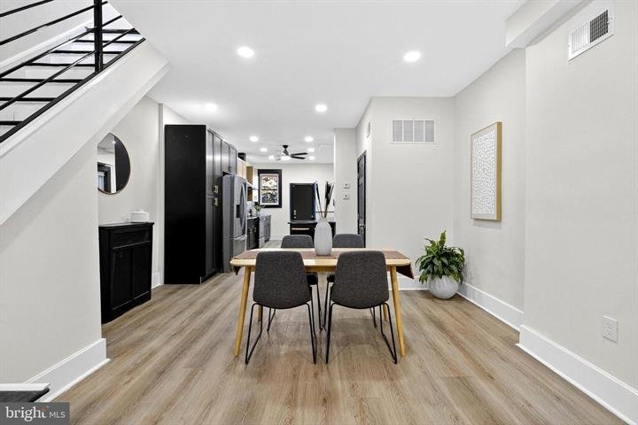 Dining table with four gray chairs, with a kitchen and staircase beyond