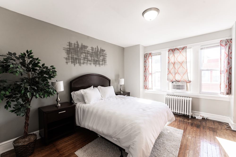 Bedroom with a queen bed, white bedding, nightstands and tall windows